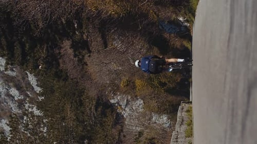 Vertical shot cyclist rides on a mountain road among high mountains, a lone sportsman cycling
