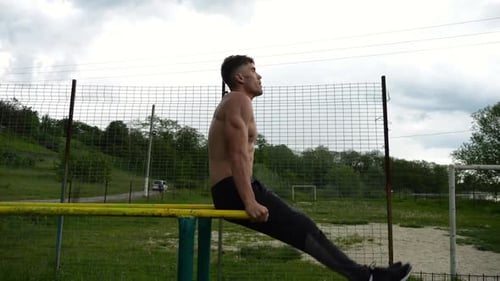 Un homme fort entraîne ses muscles abdominaux en soulevant les jambes sur des barres parallèles sur un terrain de sport pour jeunes torse nu