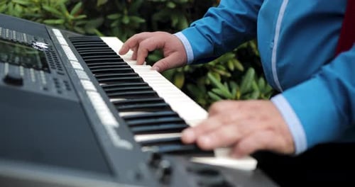 Medium Shot Of A Man With Blue Shirt Playing A Synthesizer Keyboard In The Garden
