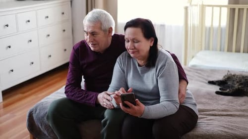 Senior Couple Sharing Smart Phone On Bed