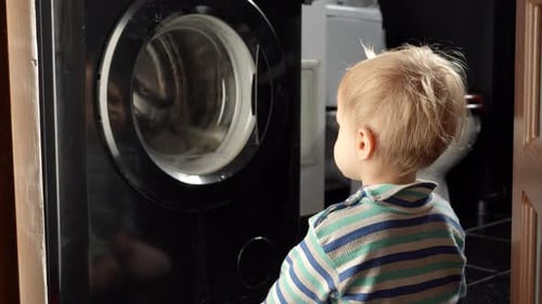 Netter kleiner Junge sitzt im Badezimmer und schaut auf die funktionierende Waschmaschine