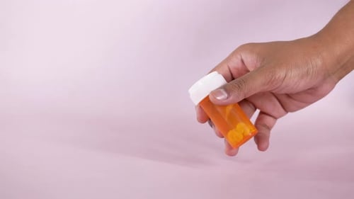 Hand Holding Orange Medicine Bottle With Pills