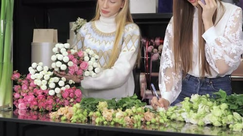 Two Workers Female Florists Standing at a Table in Flower Workshop Holding a Bouquet of Flowers and