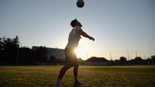 Silhouette d'un sportif pratiquant des figures avec une balle sur la tête sur le terrain au coucher du soleil, homme professionnel