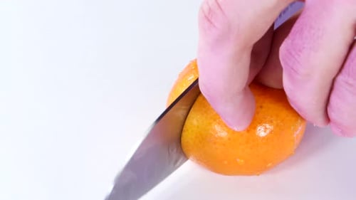 Very sharp knife cutting a thic slice of tangerine in white surface. Chopping, slicing. Close up.