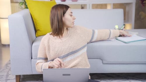 Young female college student learning online using laptop, taking notes at home.