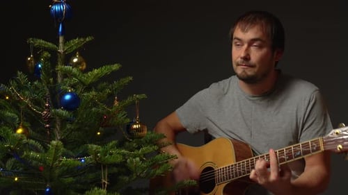 Man Plays Guitar by Decorated Christmas Tree