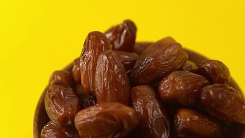 Dates fill a wooden bowl against yellow backdrop