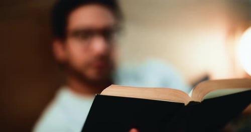 Man Reading a Book Indoors Under Warm Lighting