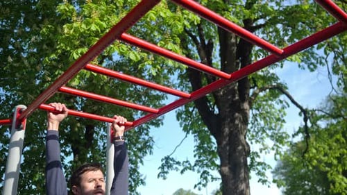 Man Training on Monkey Bars in Outdoor Fitness Park
