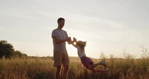 Happy Father Spinning His Daughter Holding Hands in a Golden Field at Sunset