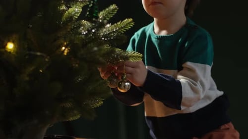 Child Decorates Small Christmas Tree with Baubles