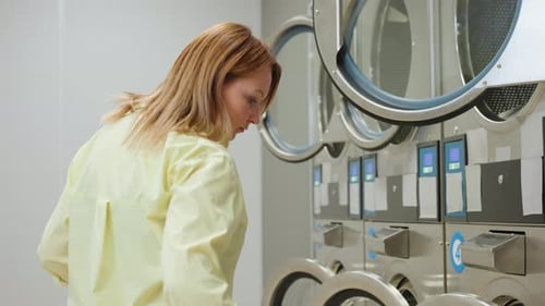 Young Woman Arranging Industrial Washing Machine in Laundromat Close Up