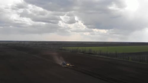 Blue tractror planting sunflower with yellow planter on the cultivated field in Ukraine