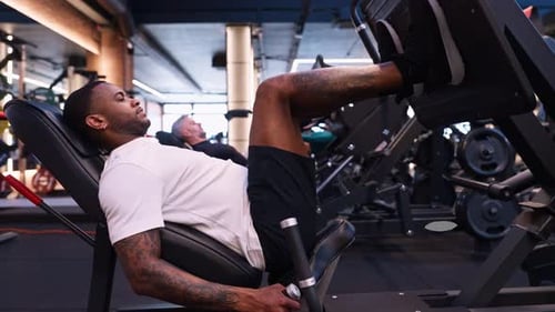Strong African American Man Training Legs on a Leg Press Machine in a Modern Gym