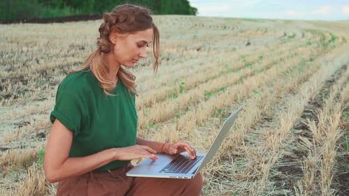 Female Agronomist Using Laptop While Examining Field