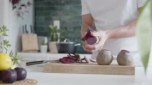 Close-up of a man peeling fresh beetroot with a peeler in a modern kitchen