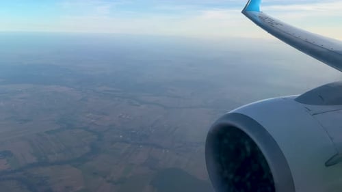 Aerial view from airplane with aircrafts turbine and wing with blue tip in foreground. Polish rural