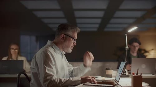 Empresário sênior trabalhando no laptop no escritório à noite