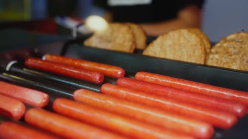 Sausages and Patties on Grill Against Man in Cafe Closeup