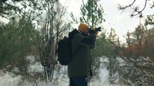 Man Taking Pictures with DSLR Camera in Snowy Forest