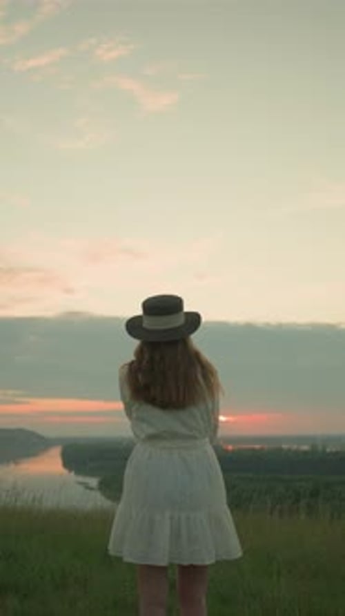 Woman in White Dress Gazing at Tranquil Lake During Serene Sunset in Grassy Field