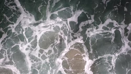 Stormy sea with waves breaking, white foam and beach sand dragged into the sea