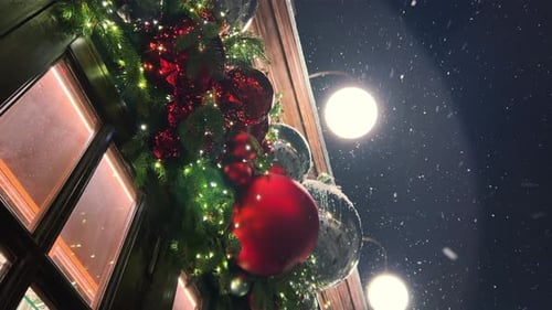 Snow falls against the background of green coniferous branches and red Christmas decorations
