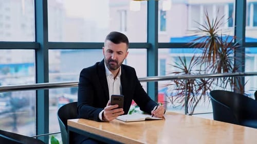 Serious focused businessman uses smartphone sitting at the desk.