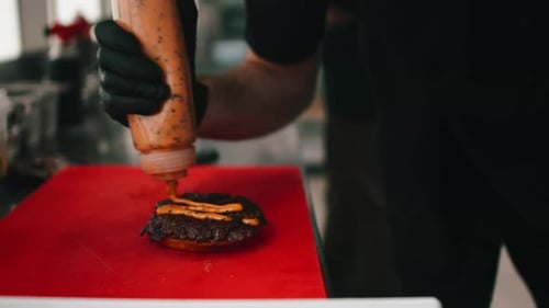Chef Adding Sauce to Burger in Restaurant Kitchen