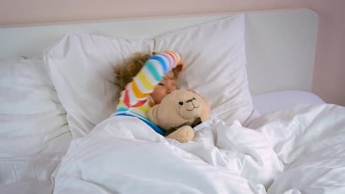 Blonde Child Wakes in White Bed with Teddy Bear