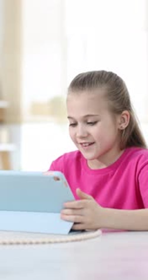 Little girl using modern tablet at white marble table indoors