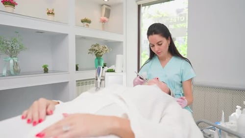 Woman Beautician Makes Rejuvenating Facial Skin Procedure of a Female Client