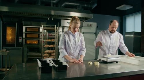 dos panaderos dan forma a la masa cruda antes de hornearla, la cortan y la despliegan sobre la mesa de cocina profesional