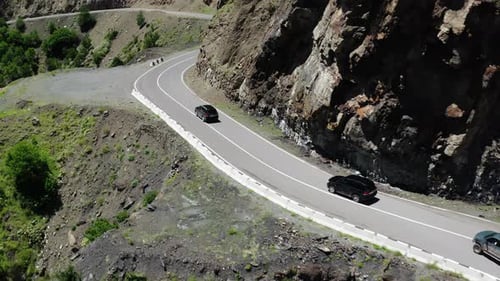 Curved Mountain Road Hugging Rocky Cliffs with Vehicles in a Lush Green Environment