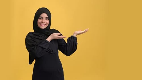Smiling Beauty Oriental Woman in Black Hijab Showing Copy Space Advertising Isolated Orange Studio
