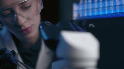 Female Scientist Using Microscope in Dark Lab