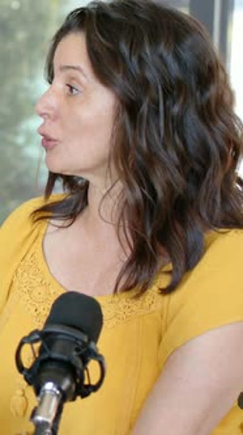 Vertical video: Answering interviewer cue, woman wearing yellow blouse speaking into mic at home