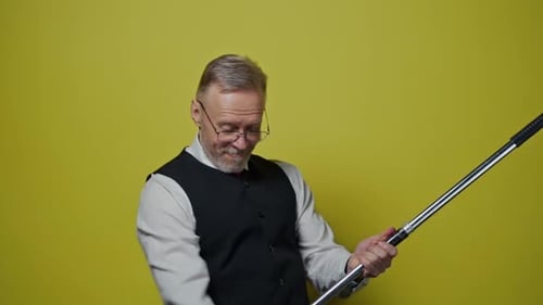 Mature Man Playing Mop Guitar on Yellow Background
