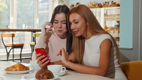 Two Women in Cafe Looking at Smartphone