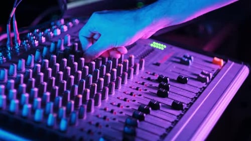 Male Hand Adjusting Faders Up And Down on Audio Mixer in Neon Light CloseUp
