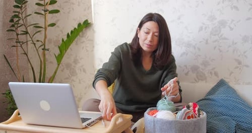 Woman Crochets at Home with Laptop