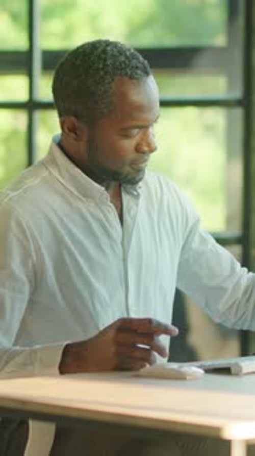 Man Reads Paperwork and Types at Computer