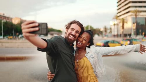 Closeup of smiling interracial couple taking a selfie on fountain background