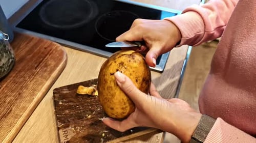Closeup view of peeling of raw potato by a woman.