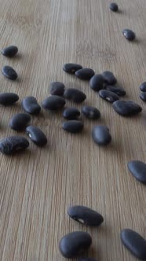 Vertical Video of Falling Black Beans in Wooden Table