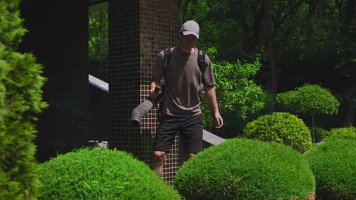 Gardener Using Professional Leaf Blower to Clear Foliage From Shrubs and Plants Essential Landscape
