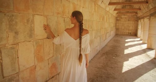 Female tourist touching historic stone wall inside archaeological structure of Mayan ruins
