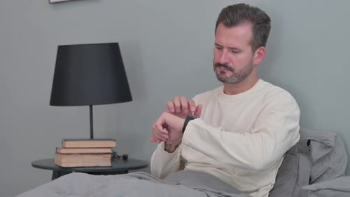 Man in Bed Looking at Smart Watch