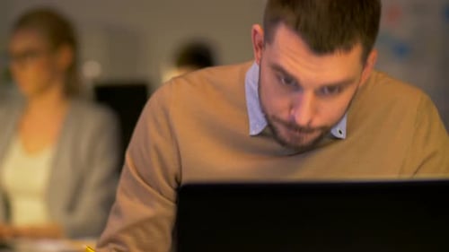 Hispanischer Geschäftsmann überlastete mit Laptop und Kollegen, die spät in der Nacht arbeiteten